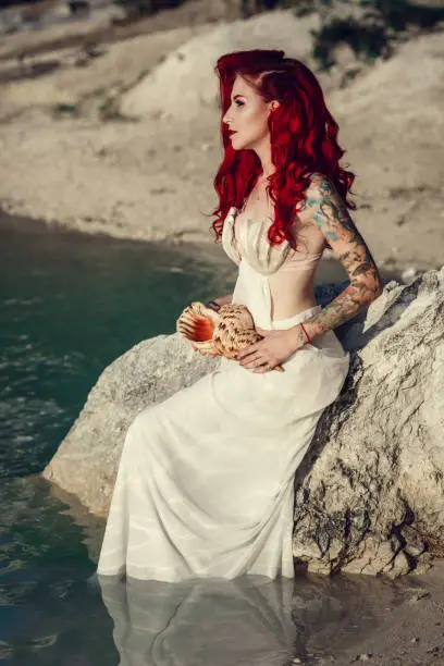 Beautiful young woman with red hair by the sea. Cosplay on a mermaid Ariel