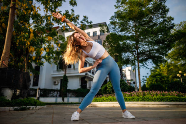 Morning Exercise in a City Park A young woman stretching before exercise and jogging outdoors in a park by Tay Ho Lake (West Lake) in Hanoi, Vietnam legs apart stock pictures, royalty-free photos & images