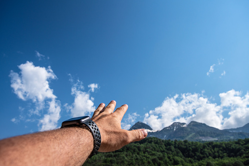 Man's hand reaches for the top of the mountain at sunny day