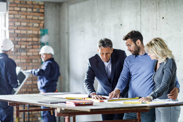 istock Young couple and their agent examining blueprints at construction site. 1368328626