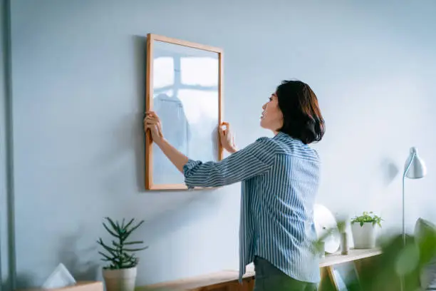 Photo of Young Asian woman decorating and putting up a picture frame on the wall at home