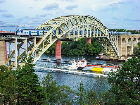 Scandinavian Metro train on bridge with loaded barge passing on waterway underneath