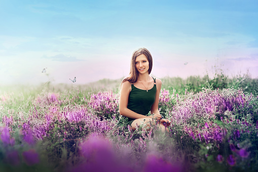 girl in a green dress on the summer field. Blue sky, butterflies fly