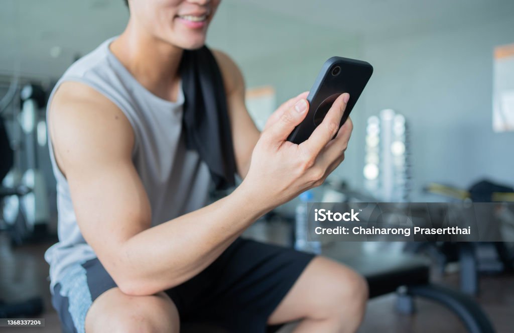 close up young asian man use smartphone to check news on social media or chat with friends using rest after workout in gym for health and modern lifestyle concept Gay Person Stock Photo