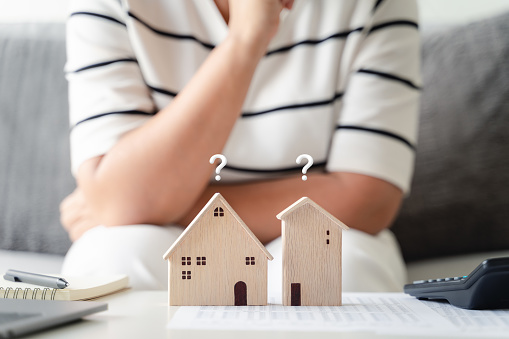 woman is deciding to choose house with Small Wooden House Model with Question Marks, Planning to buy property. Choose what's the best. home loan concepts.