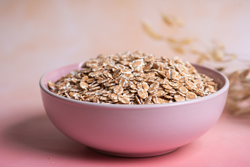 Bowl with oatmeal flakes on a pastel pink background.Top view.Stock photo.