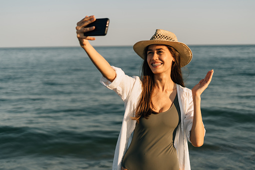 Close-up portrait of a girl on the ocean. Wearing a straw hat, she is holding a smartphone and making a video call using an app on her smartphone. accessible internet concept. Banner. copy space