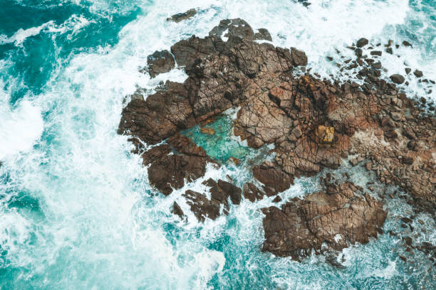 Aerial drone shot of ocean waves around rocks and rock pool Aerial drone shot of ocean waves around island of rocks and rock pool tidal pool stock pictures, royalty-free photos & images