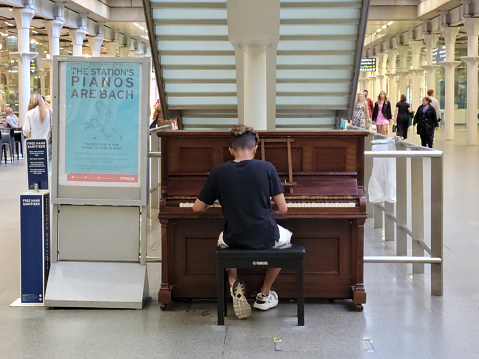 Public piano being used in St Pancras International rail station in London, England, UK.