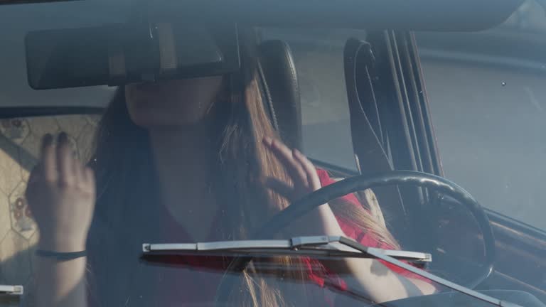 Variants of behavior of people behind the wheel of a car. A young woman gets behind the wheel of an old car and immediately looks in the rearview mirror and preens