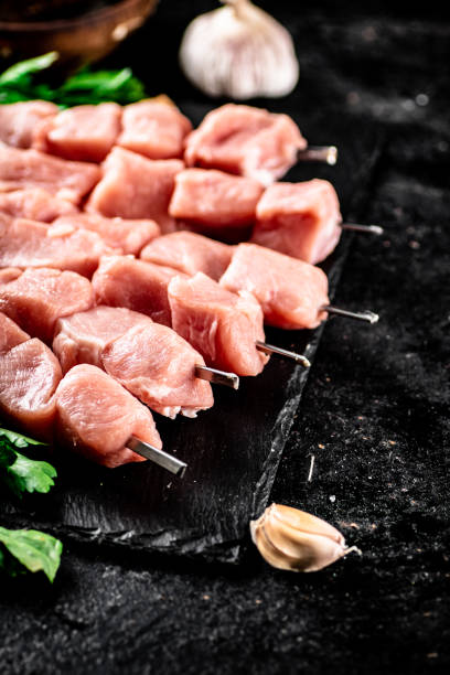 istock Pork kebab raw with greens and garlic on a stone board. 1368356333