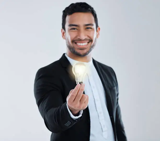 Photo of Shot of a young man holding a light bulb against a grey background