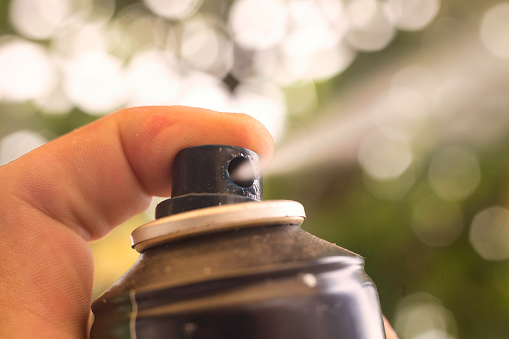 A finger presses the nozzle on an aerosol can causing a spray