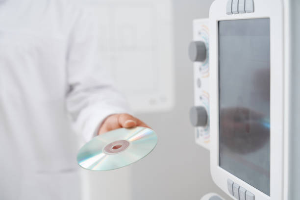 Crop of male doctor holding plate with silver CD plate with information and results after ultrasound diagnostic. Usg equipment in modern clinic.