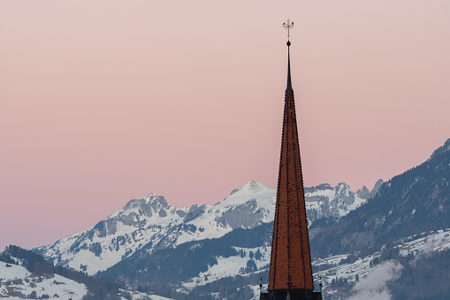Schaan, Liechtenstein, January 19, 2022 Tower of the catholic church in front of the majestic swiss alps in the morning time