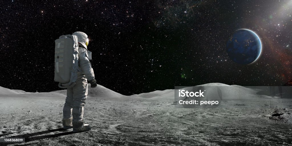 Astronaut Standing On The Moon Looking Towards A Distant Earth A lone astronaut standing facing away from the camera dressed in full space suit with backpack, stands still looking towards a distant planet Earth. The sun illuminates a side of Earth and hundreds of stars are visible in deep space. Moon Surface Stock Photo