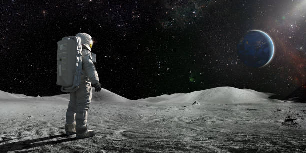 Astronaut Standing On The Moon Looking Towards A Distant Earth A lone astronaut standing facing away from the camera dressed in full space suit with backpack, stands still looking towards a distant planet Earth. The sun illuminates a side of Earth and hundreds of stars are visible in deep space. moon surface stock pictures, royalty-free photos & images