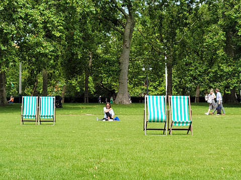 Deckchairs for hire and people on the grass in St James's Park in London, England, UK.