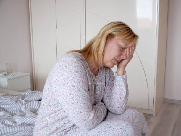 istock sick sad woman holding her sore head while sitting on bed 1368369786