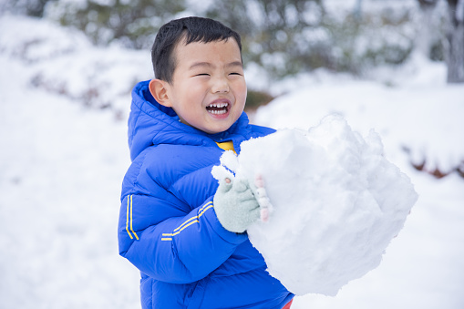 Little boy holding snowball in winter