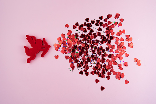 Angel cupid shots tiny red heart-shaped confetti on a pink background. Valentine's day - concept. Directly above shot.