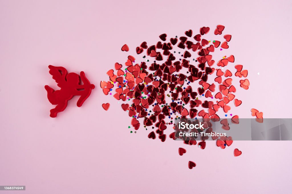 Happy saint valentines day Angel cupid shots tiny red heart-shaped confetti on a pink background. Valentine's day - concept. Directly above shot. Cupid Stock Photo