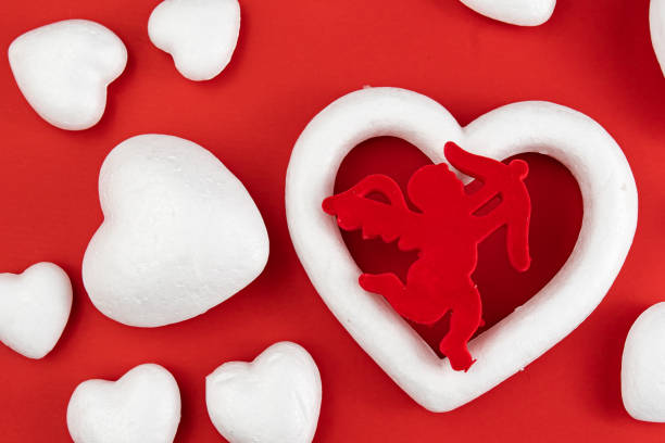 Angel Cupid with white heart-shaped Styrofoam, red background. Valentine's day celebration concept. Directly above shot.