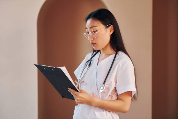 istock Holds notepad in hands. Young serious asian woman standing indoors 1368376129