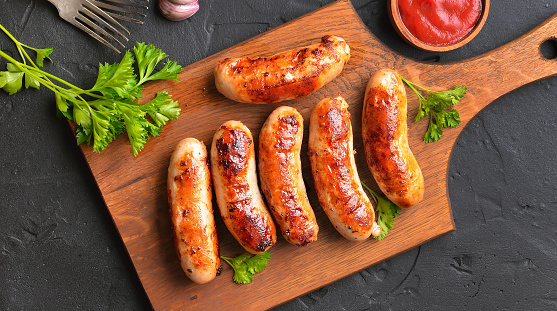 Roasted sausages on cutting board over dark background. Top view, flat lay