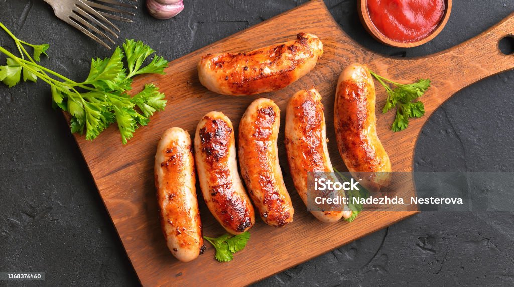 Roasted sausages on cutting board Roasted sausages on cutting board over dark background. Top view, flat lay Sausage Stock Photo