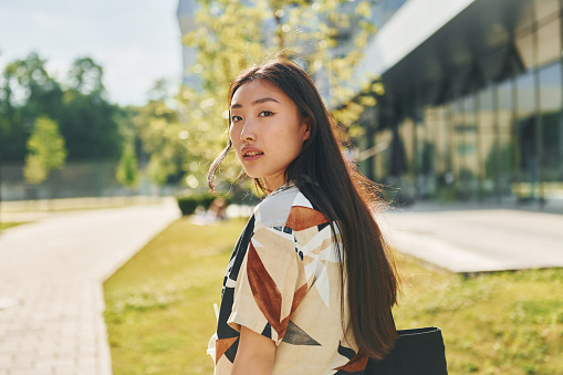 Student walks near modern building. Young asian woman is outdoors at daytime.