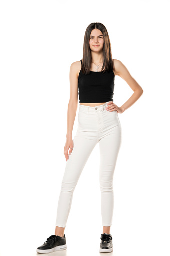 a teenage girl in white jeans and a black shirt stands on a white background