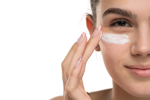 portrait of a young smiling teen girl applying cosmetic product under her eyes on a white background