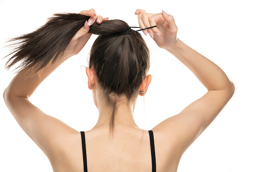 Rear view of a young woman tying her long hair on white background