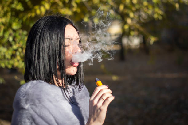 the girl smokes an electronic cigarette on the street. - vape stockfoto's en -beelden