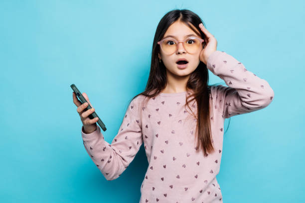 istock Caucasian kid girl against blue wall hold hand modern technology use touch face palm astonished impressed scream wow omg 1368384463