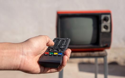 Man's hand holding remote control in front of vintage old TV