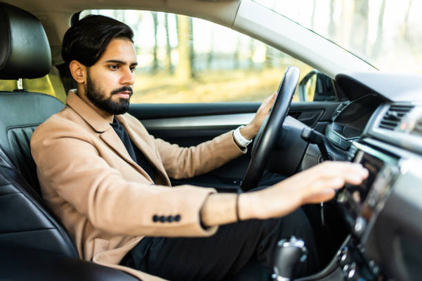 istock Handsome indian young man in denim shirt pressing touchscreen on car multimedia panel, switching shifting radio station. 1368388146