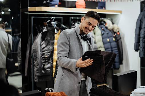 Portrait of handsome young man buying clothes in the store.sale, shopping, fashion, style and people concept - happy young man  choosing clothes in mall or clothing store