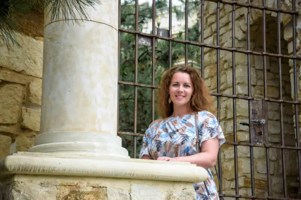 Photo of Portrait of young pretty woman on stairs near ancient historical building from stone and seashells