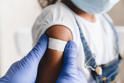 Sarampión Covid 19, ébola vacunado. Médico pediatra inyectando haciendo vacuna a niña africana en clínica médica. Enfermera que aplica el parche médico después de la inyección photo