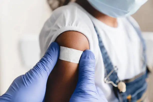 Covid 19 measles, ebola vaccinated. Doctor pediatrician injecting making vaccine to little african girl in medical clinic. Nurse applying medical patch after injection