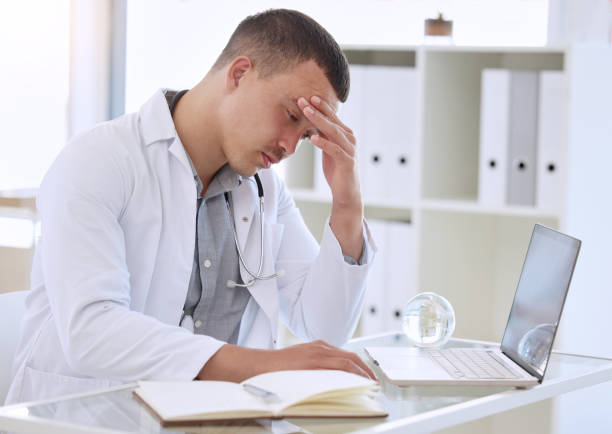 istock Shot of a handsome young doctor sitting alone in his clinic and feeling stressed while using his laptop 1368392942