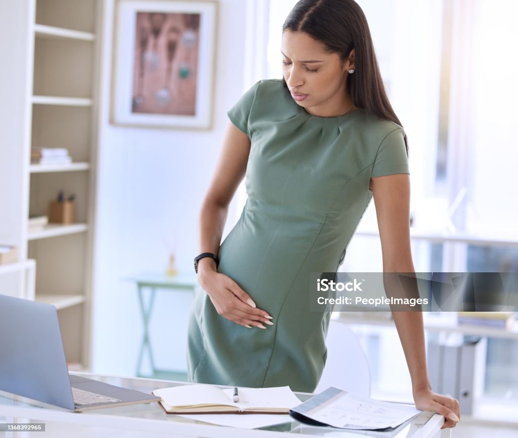 Shot of a young pregnant businesswoman standing alone in the office and suffering from abdominal pain Mommy's trying to work, little one Miscarriage Stock Photo
