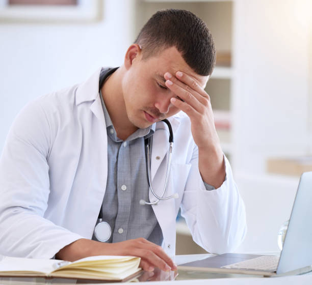 istock Shot of a handsome young doctor sitting alone in his clinic and feeling stressed while using his laptop 1368393017