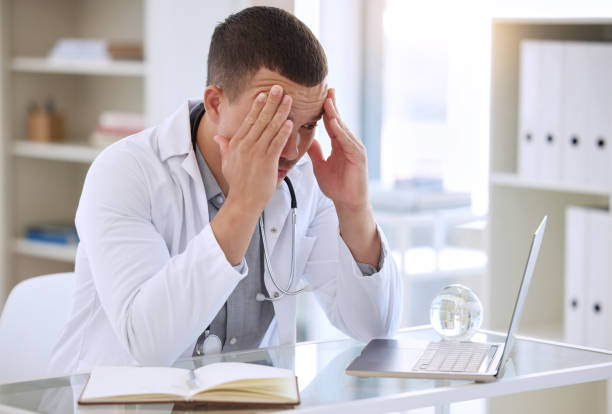 istock Shot of a handsome young doctor sitting alone in his clinic and feeling stressed while using his laptop 1368393030