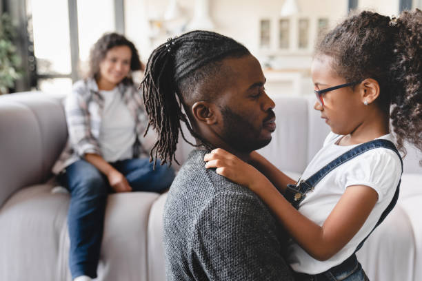 Loving african-american parents couple having fun with small preteen daughter, spending time together at home, hugging and embracing. Family bonding. Parenthood concept stock photo