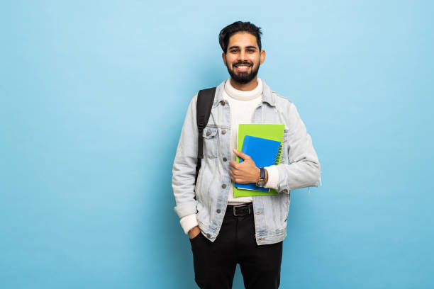 istock handsome young bearbed indian man with backpack hold books in blue background 1368394536