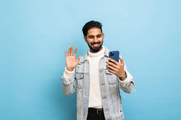 istock Handsome young Asian man with a smartphone is making a video call, isolated on blue background 1368394718