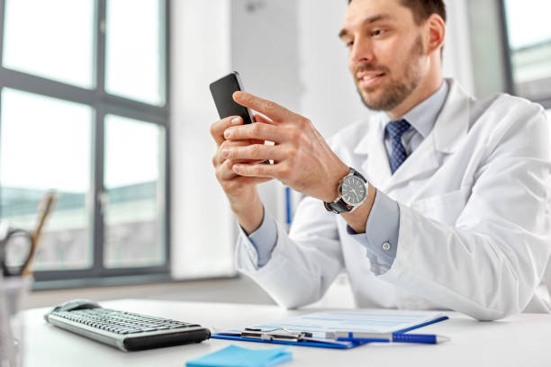 smiling male doctor with smartphone at hospital stock photo